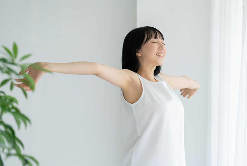 平塚市でゴミ屋敷片付け業者に依頼して、最短ルートで綺麗な部屋で気持ちよさそうに腕を広げる女性。